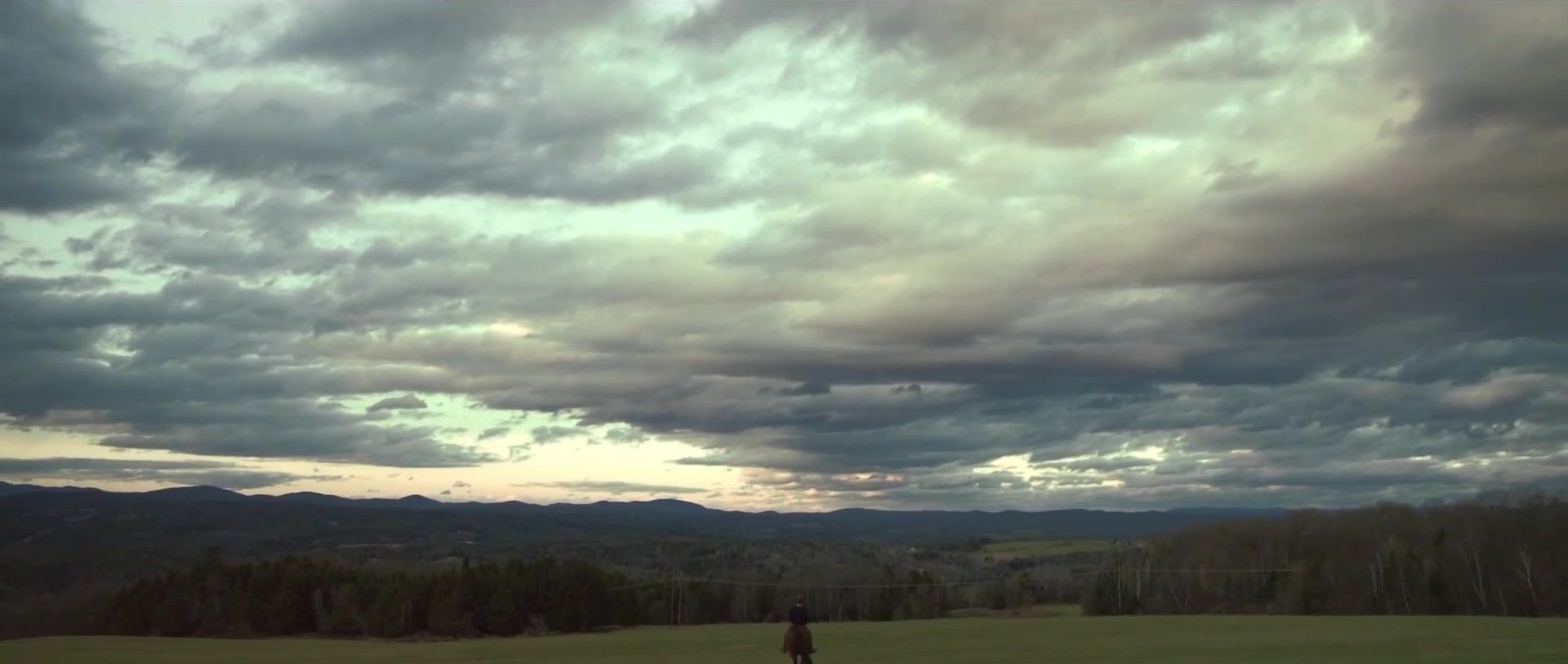 A small figure under a wide, clouded sky.