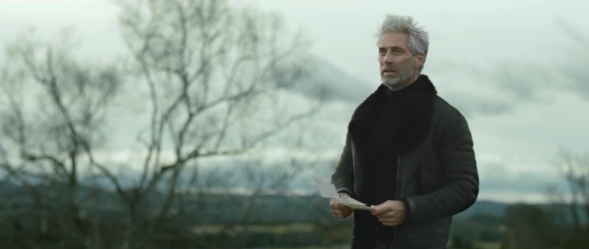 A man in open weather, holding a letter.